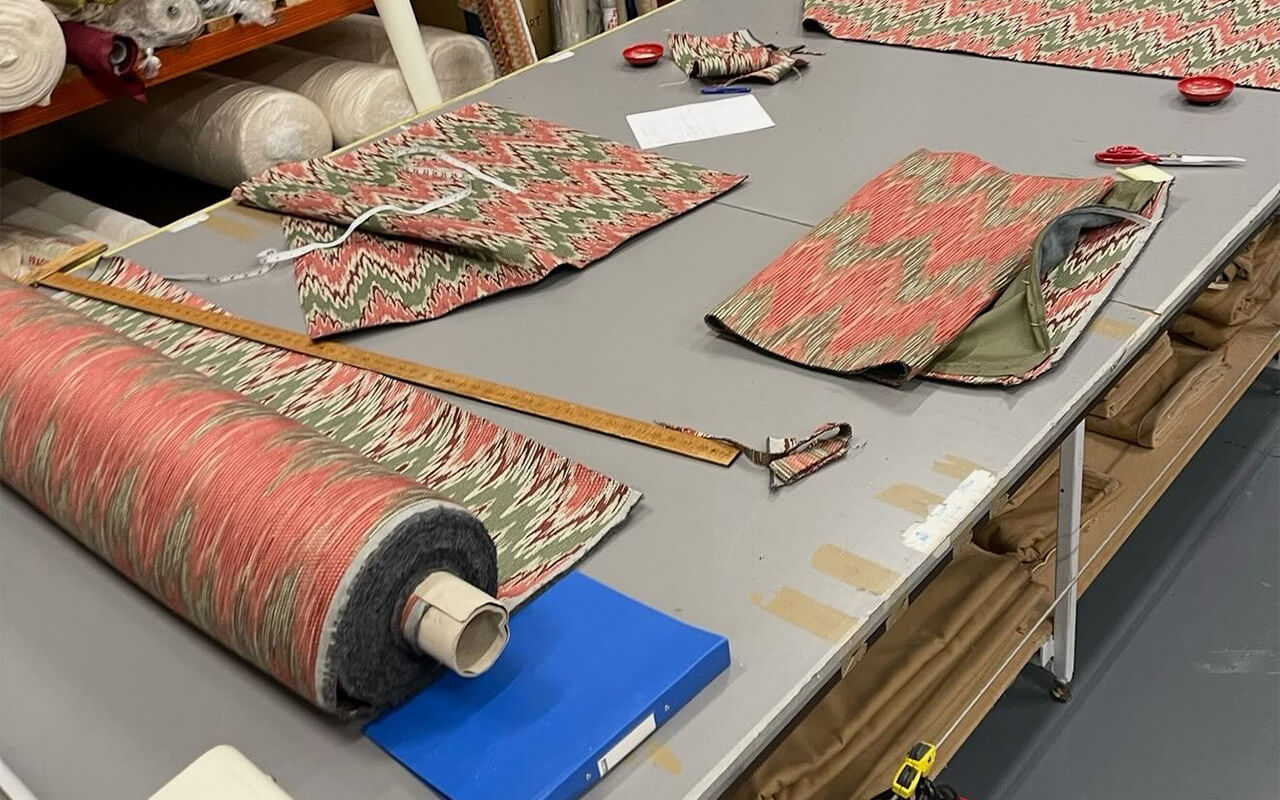 Roll of coral and green patterned fabric laid out on a large worktable alongside a wooden ruler and sewn fabric panels.